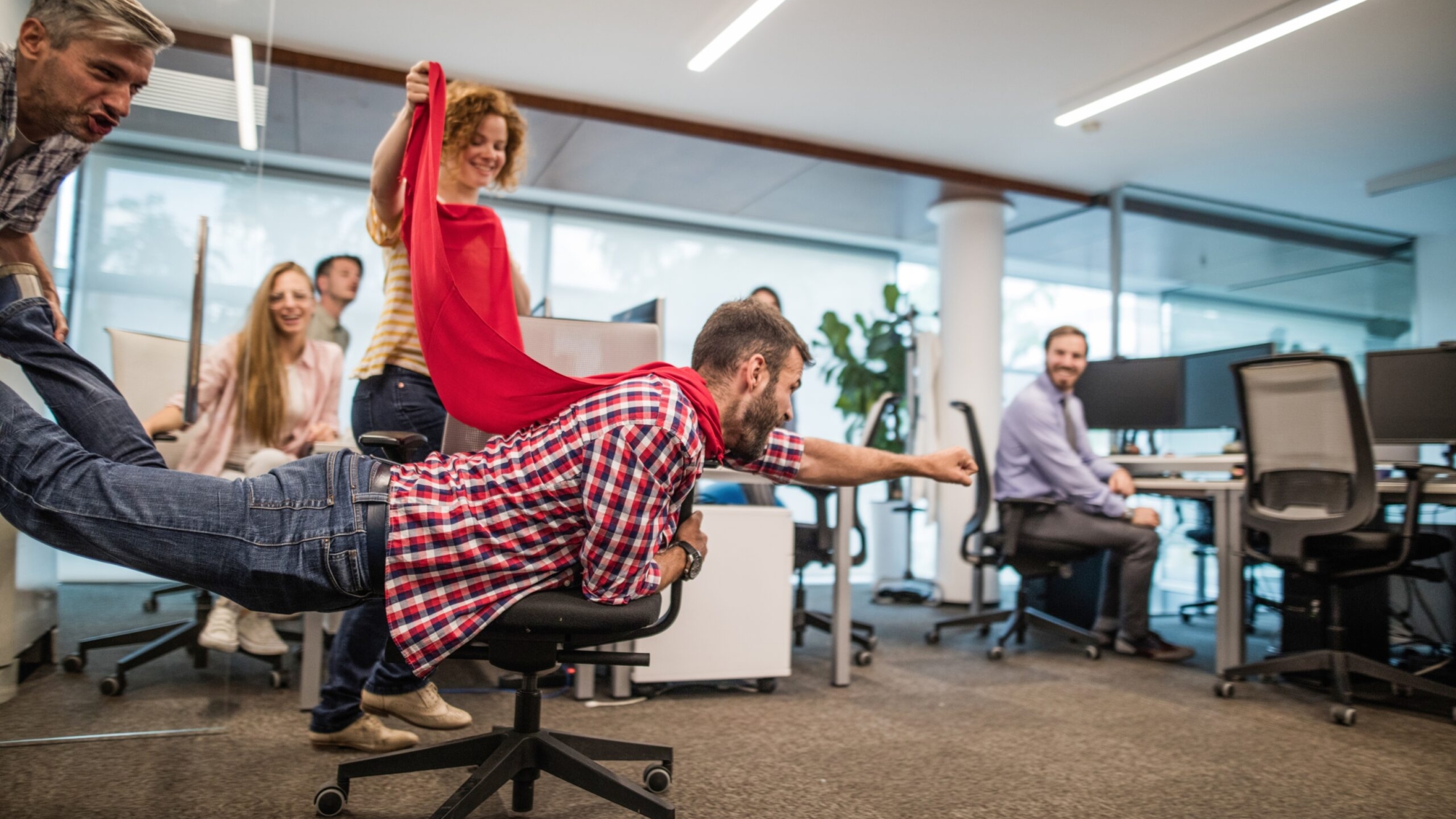 Giovane uomo che finge di essere un supereroe mentre si diverte con i colleghi durante una pausa in ufficio.