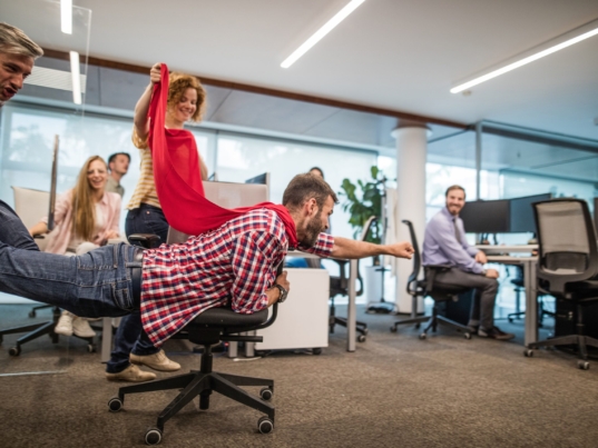 Young man pretending to be a superhero while having fun with his colleagues on a break in the office.