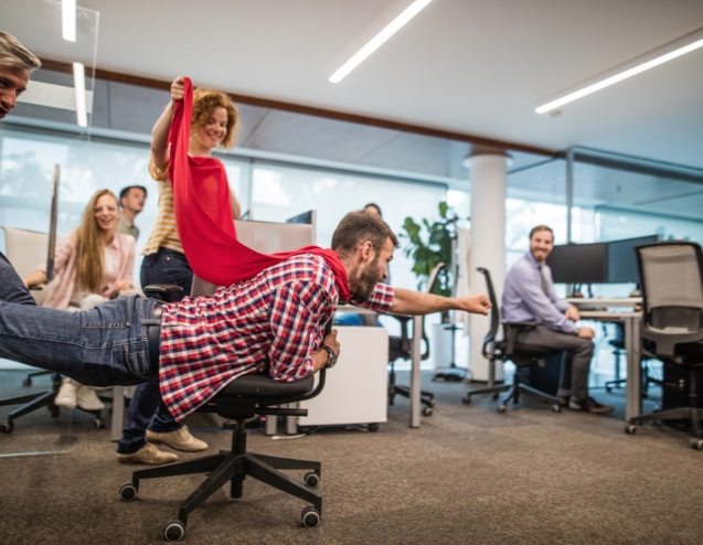 Young man pretending to be a superhero while having fun with his colleagues on a break in the office.