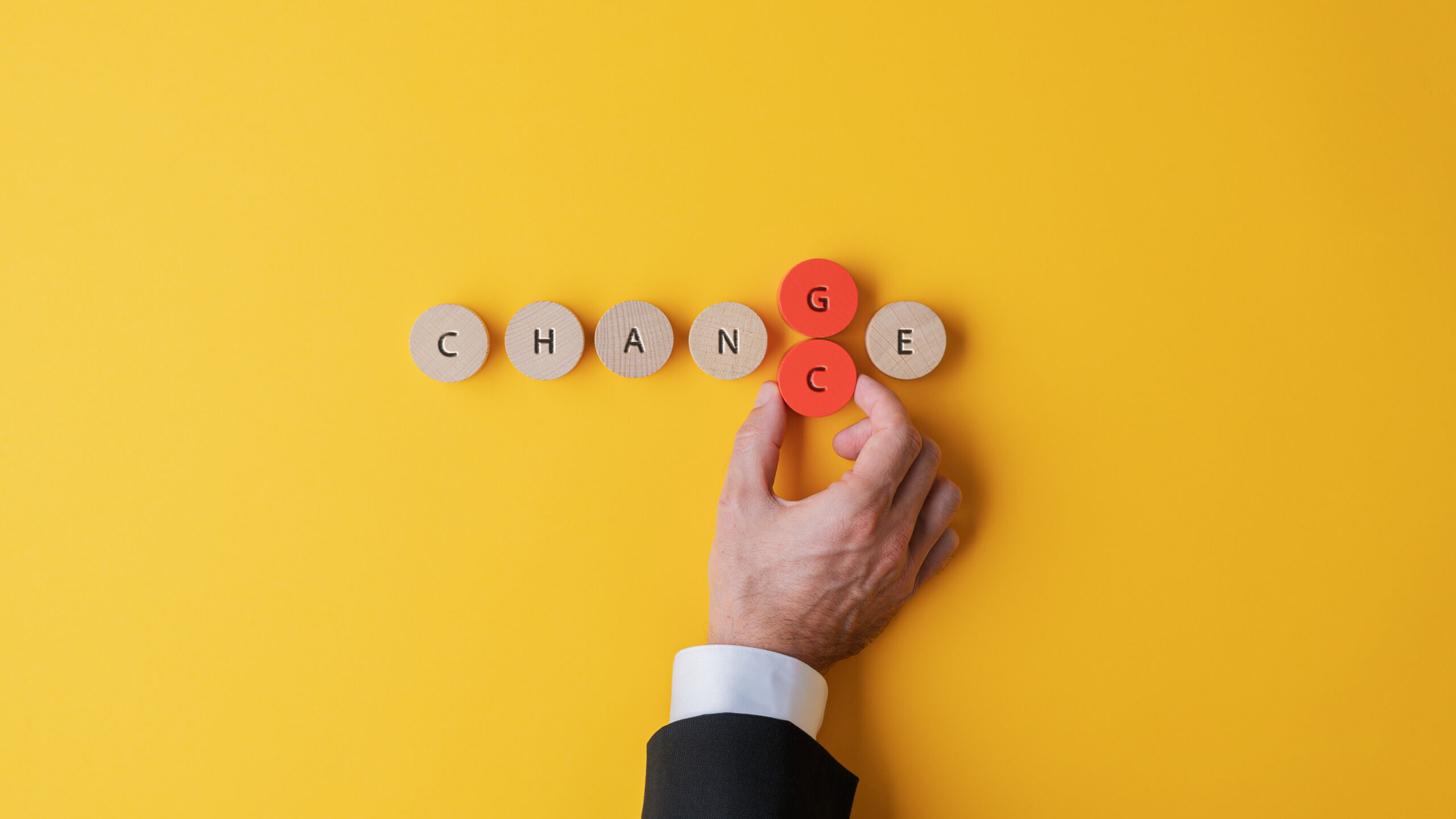 Hand of a businessman changing the letters G and C to transform a Change sign into Chance spelled on wooden cut circles.