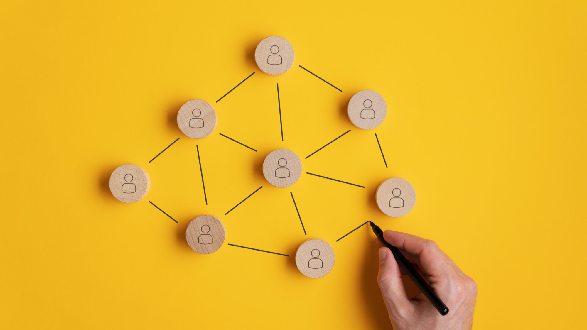 Conceptual image of network marketing - male hand connecting the wooden cut circles with person icon on them.