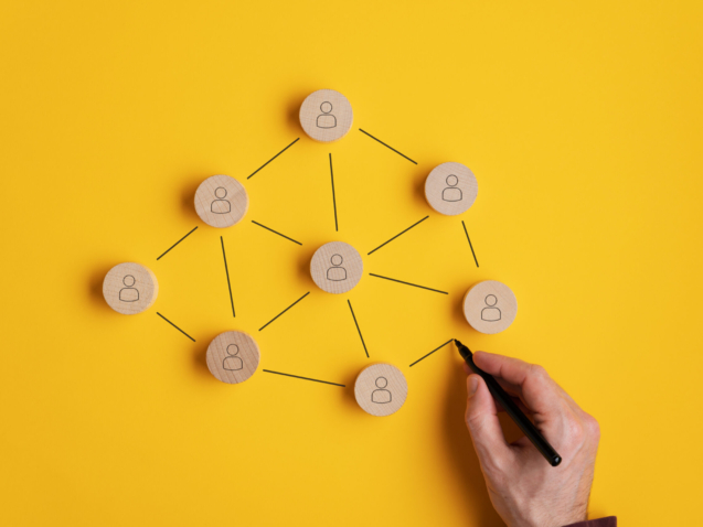 Conceptual image of network marketing - male hand connecting the wooden cut circles with person icon on them.