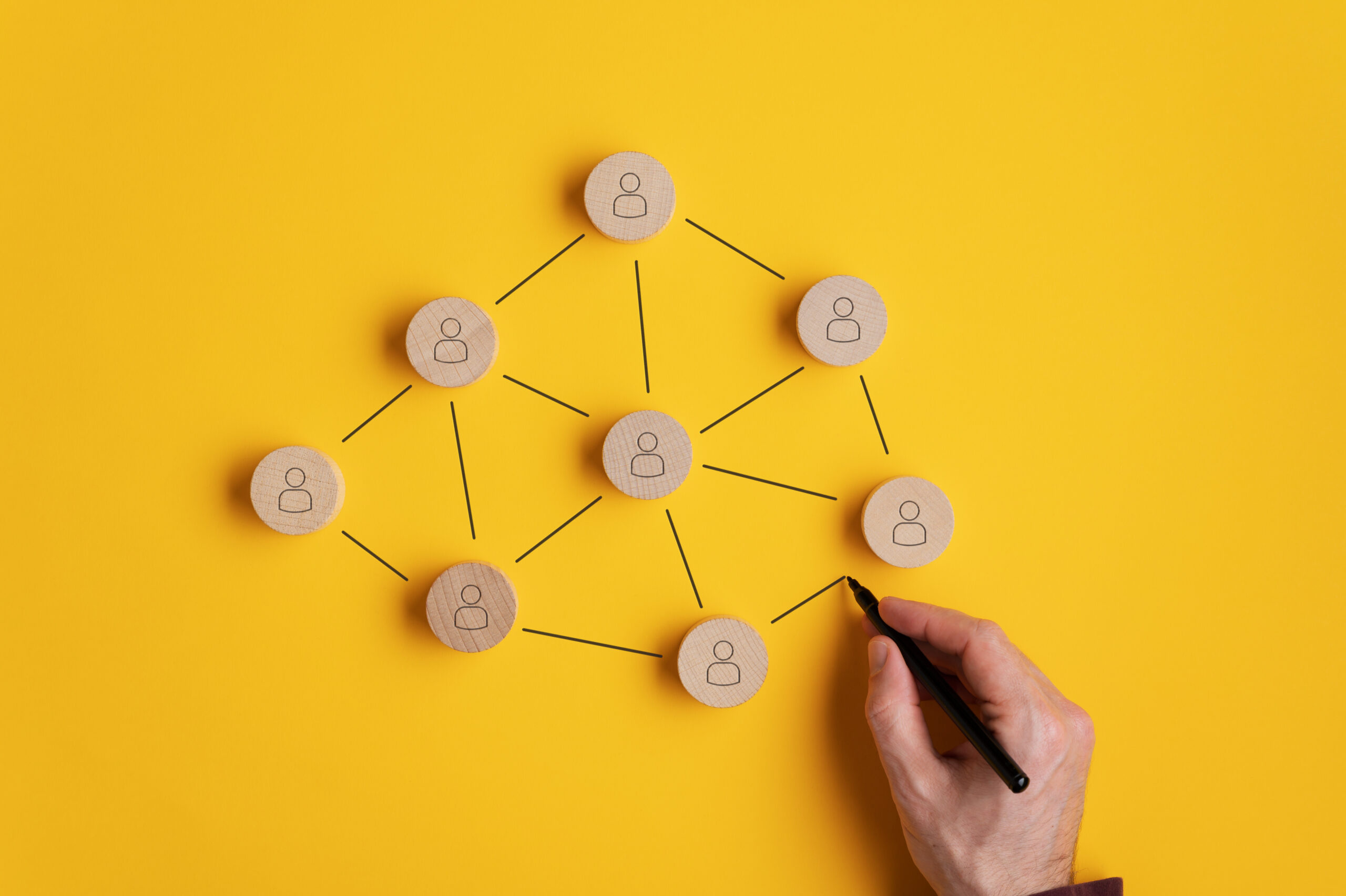 Conceptual image of network marketing - male hand connecting the wooden cut circles with person icon on them.