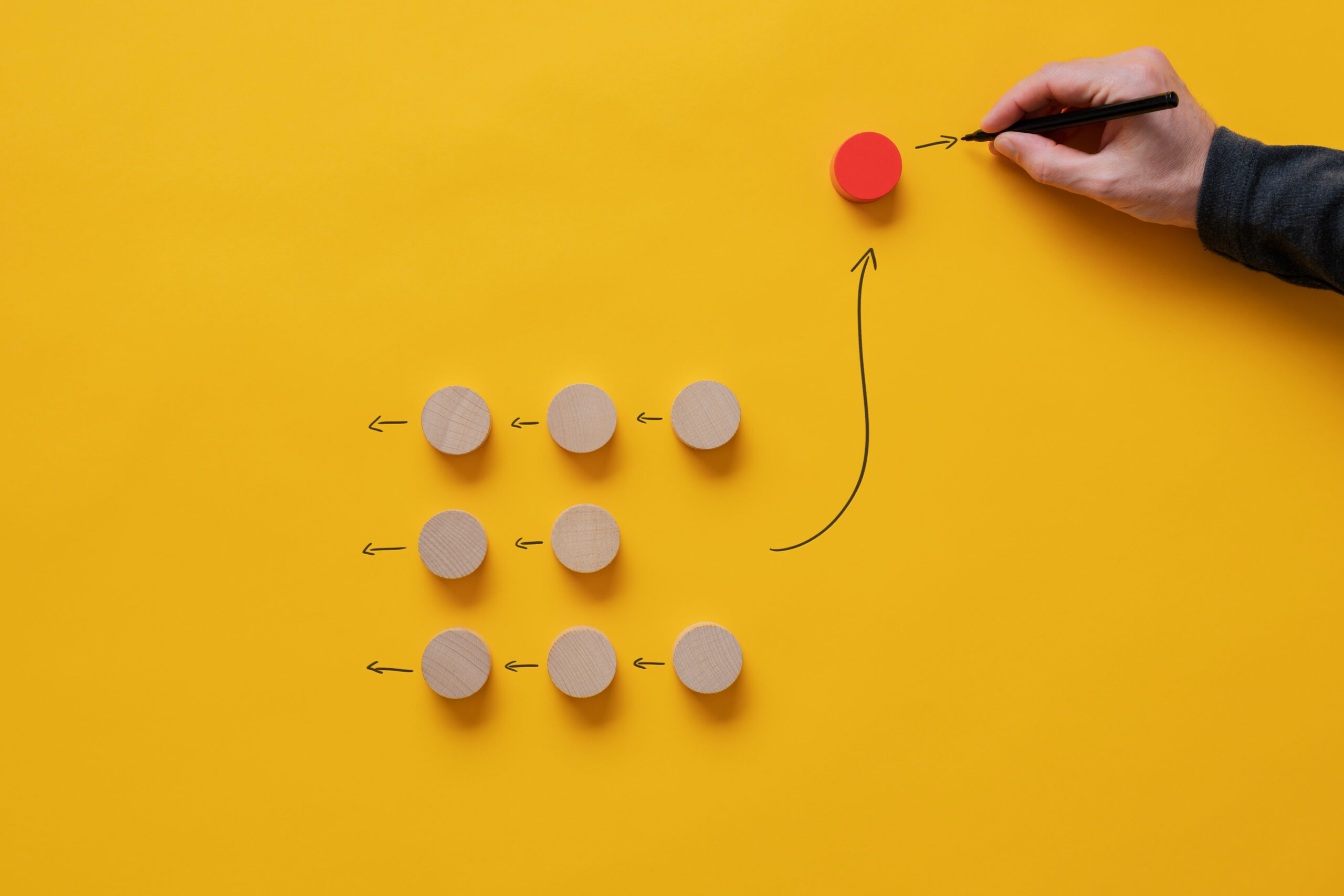 Group of wooden cut circles all heading in the same direction with one, red, turning the other way. Conceptual image of individuality and different thinking.