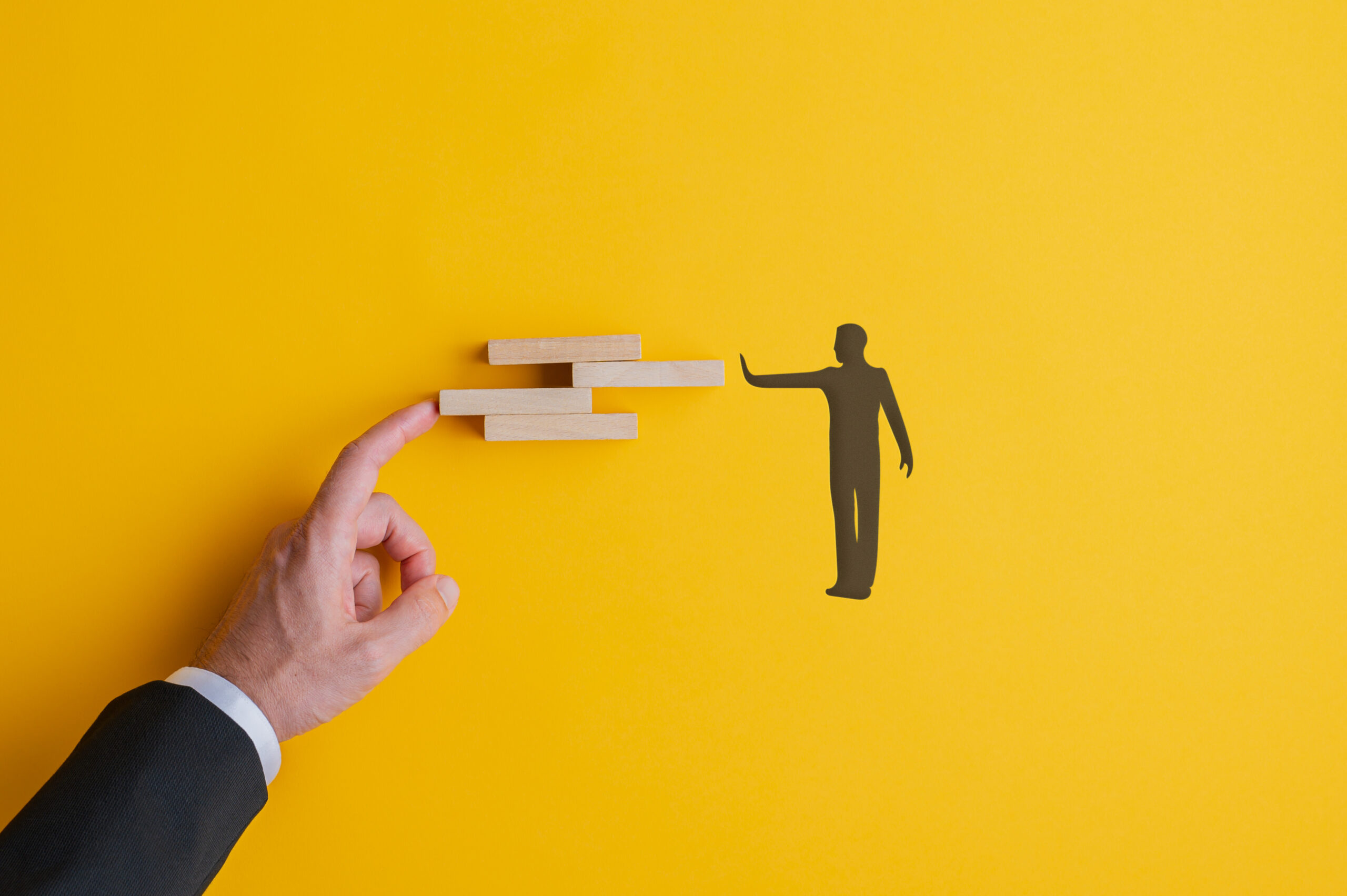 Conceptual image of teamwork and problem solving with male hand and silhouetted male figure arranging wooden blocks.